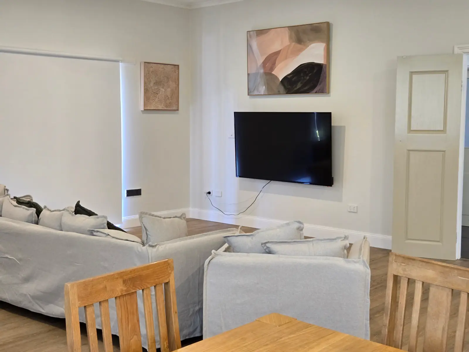 Section living room at the Ryrie Street residence with two linen sofas, framed artwork, a wall-mounted television and an adjoining timber dining table
